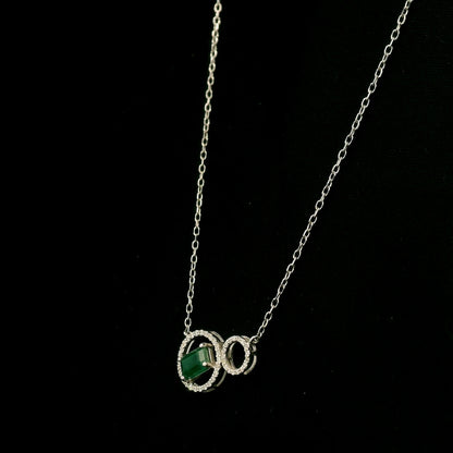 Emerald and diamond necklace in 18K white gold featuring a rectangular emerald-cut green gemstone inside a diamond circle, connected to a smaller diamond-set circle.