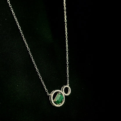Emerald and diamond necklace in 18K white gold featuring a rectangular emerald-cut green gemstone inside a diamond circle, connected to a smaller diamond-set circle.