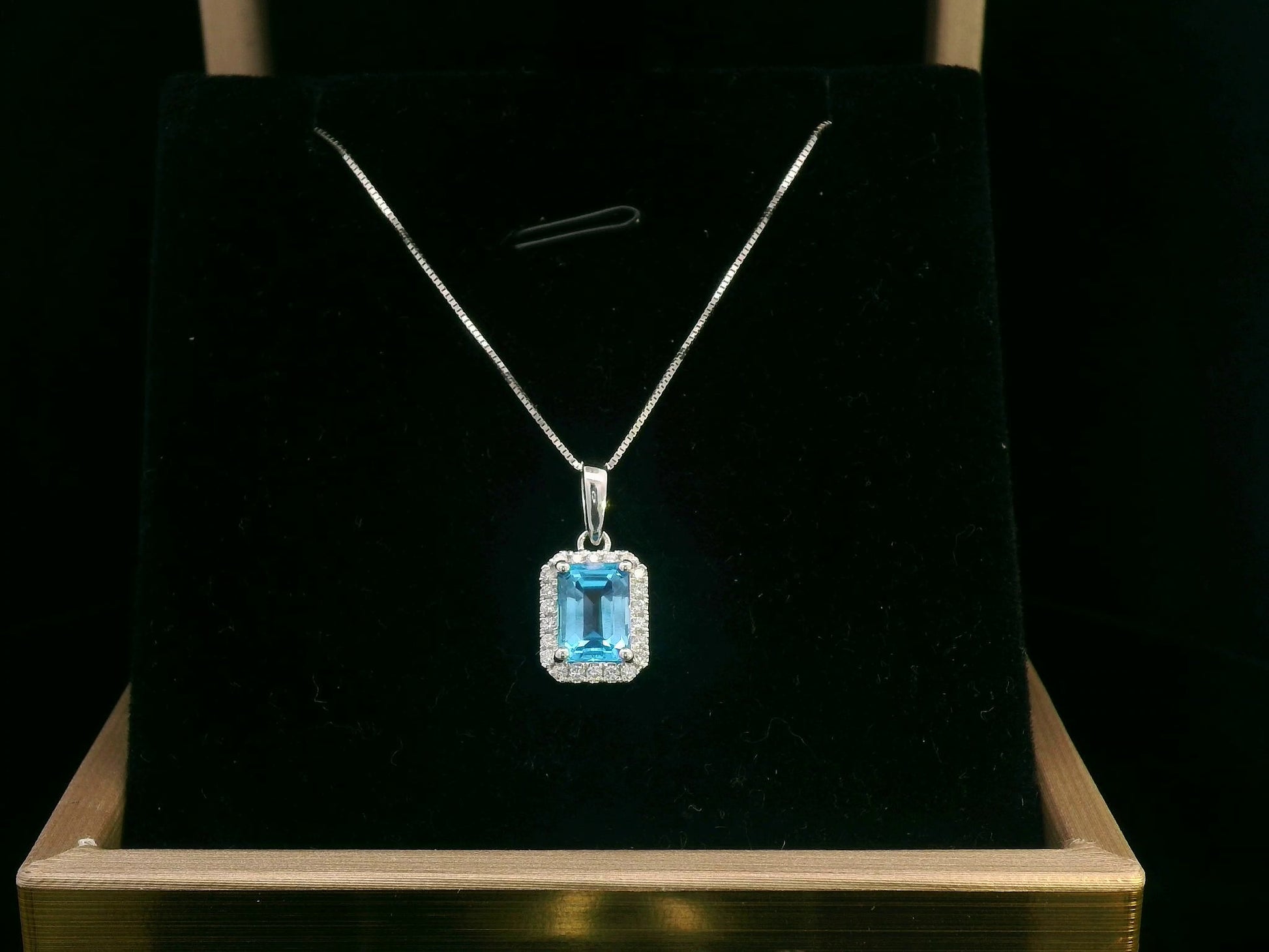 Emerald-cut blue topaz pendant with diamond halo in 18K gold, featuring a 1.40-carat gemstone and 0.13-carat diamonds.