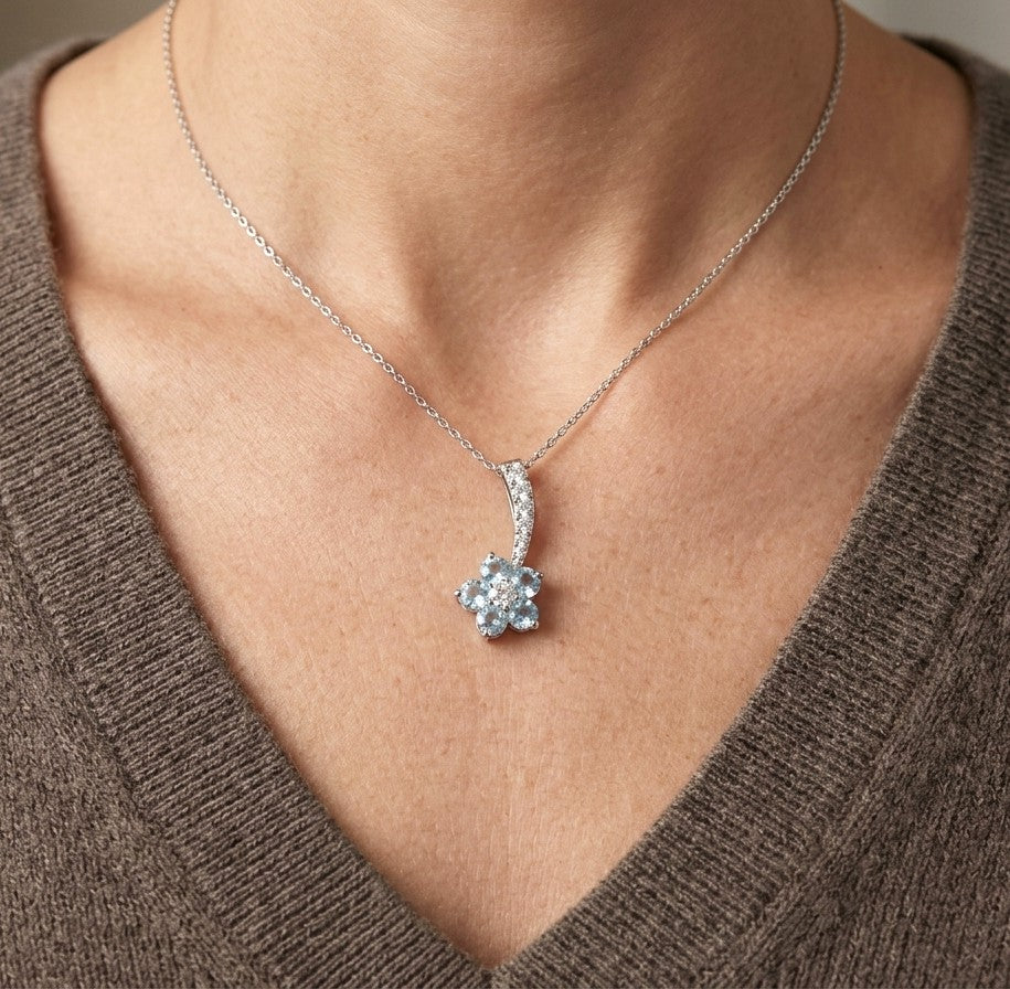 Aquamarine flower pendant in 18K white gold with five round blue gemstones, diamond centre and curved diamond-set bail.