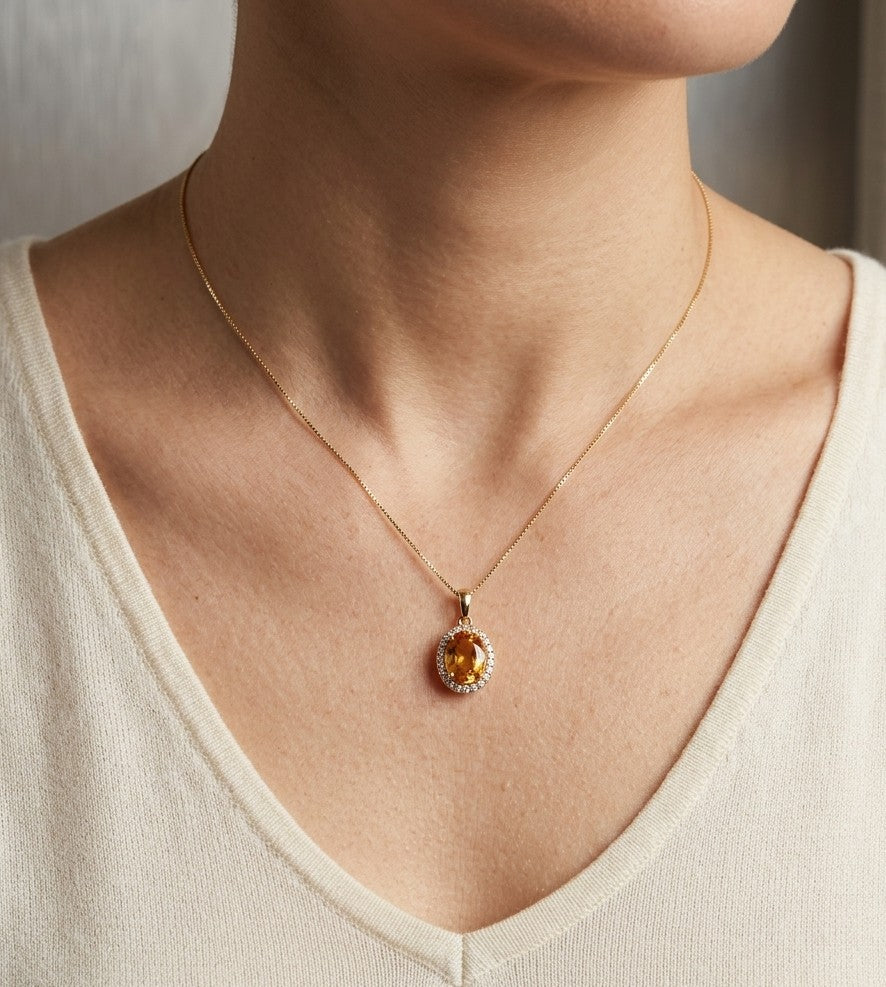 Oval golden-orange citrine pendant surrounded by a halo of round diamonds in polished 18K gold.