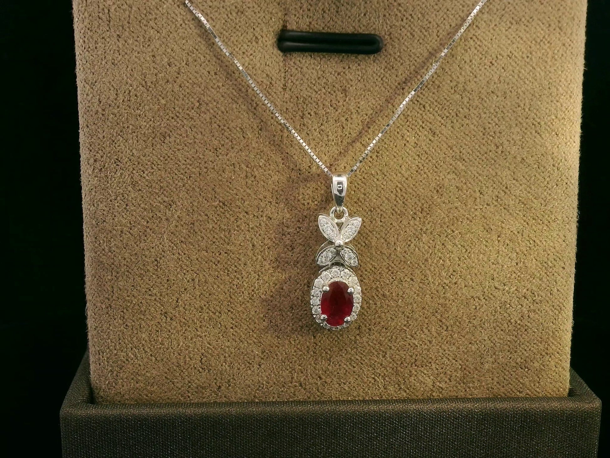 18k white gold pendant with 0.63-carat oval ruby, diamond halo, and floral diamond-accented bail