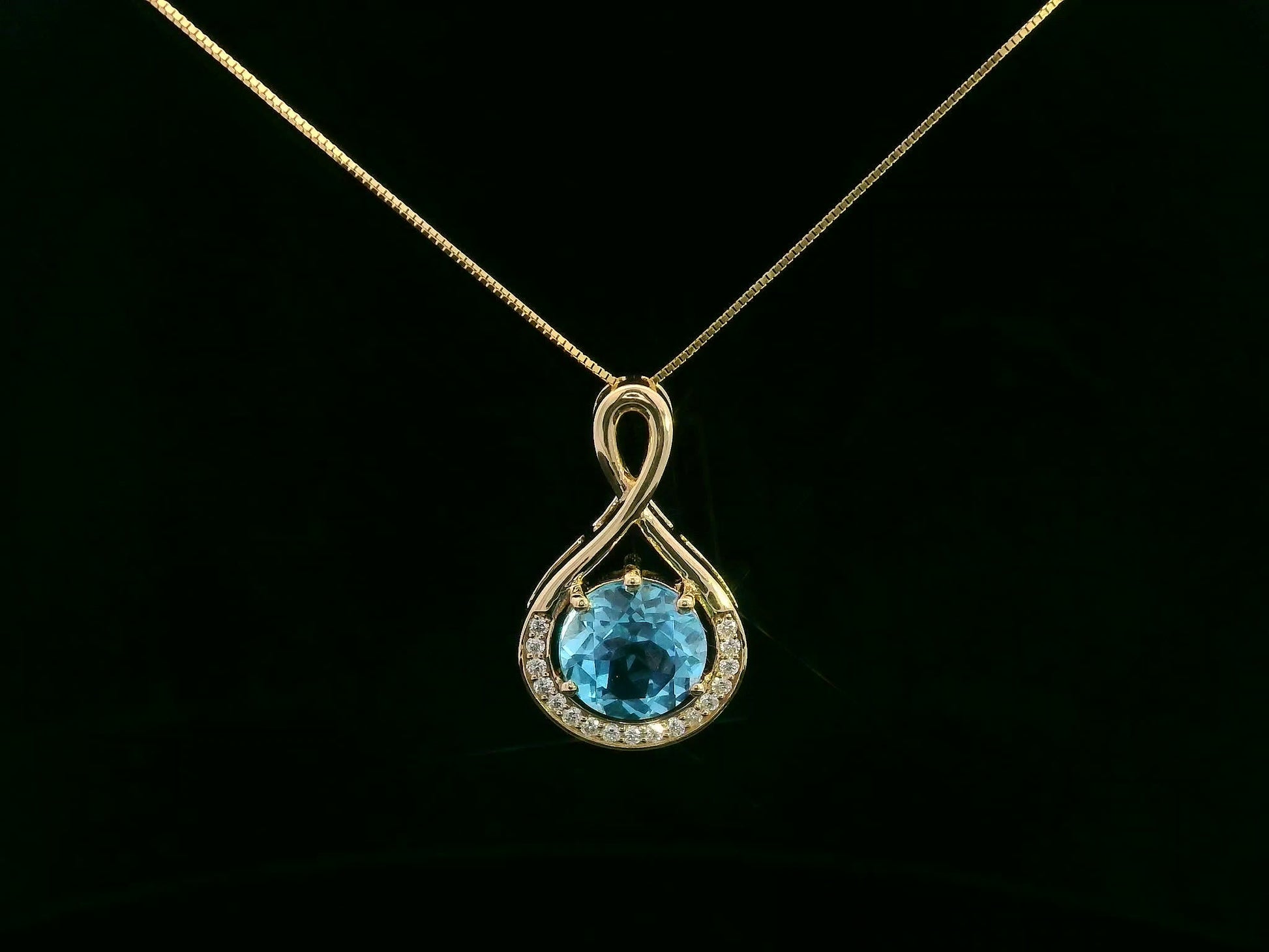 18k yellow gold pendant with 2.30 carat Swiss blue topaz center, diamond halo, and infinity-style bale