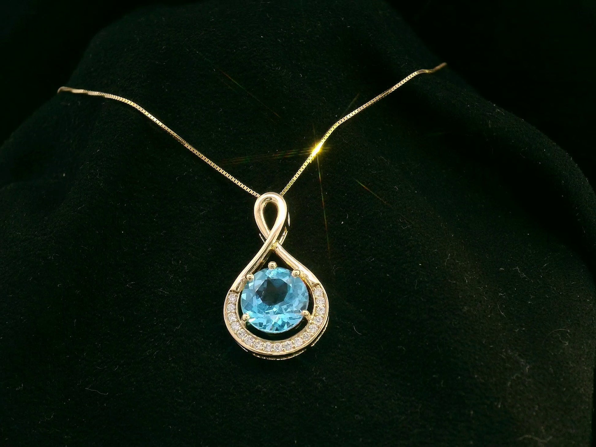 18k yellow gold pendant with 2.30 carat Swiss blue topaz center, diamond halo, and infinity-style bale