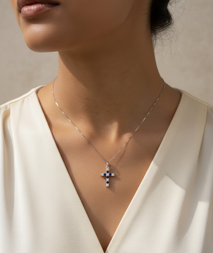 18K white gold diamond and blue sapphire cross pendant with prong-set gemstones by Emirates Diamonds.