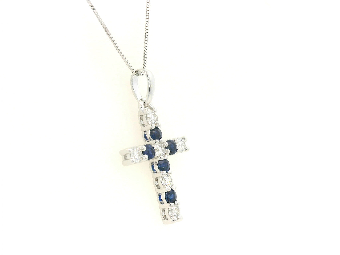 18K white gold diamond and blue sapphire cross pendant with prong-set gemstones by Emirates Diamonds.