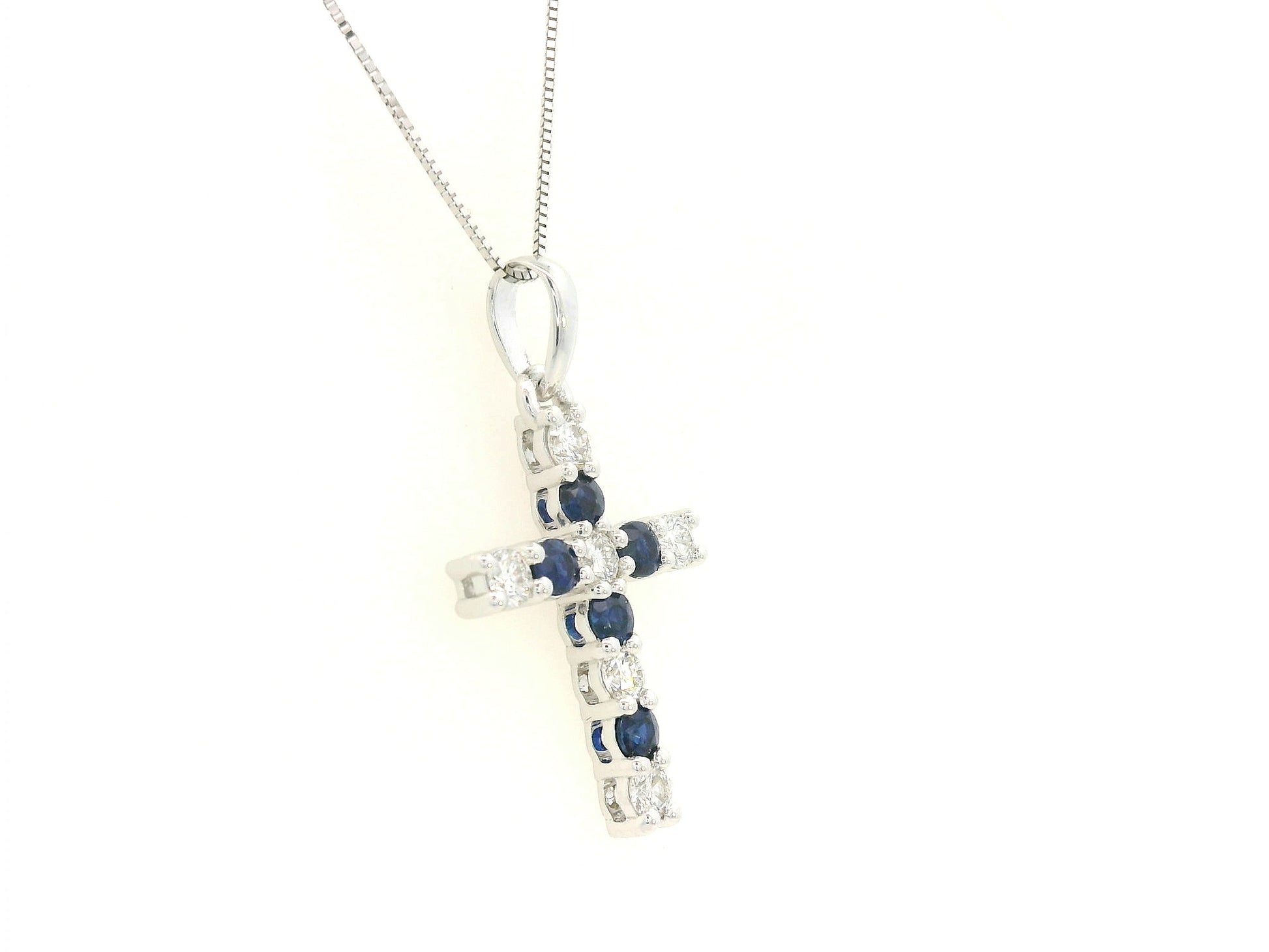 18K white gold diamond and blue sapphire cross pendant with prong-set gemstones by Emirates Diamonds.