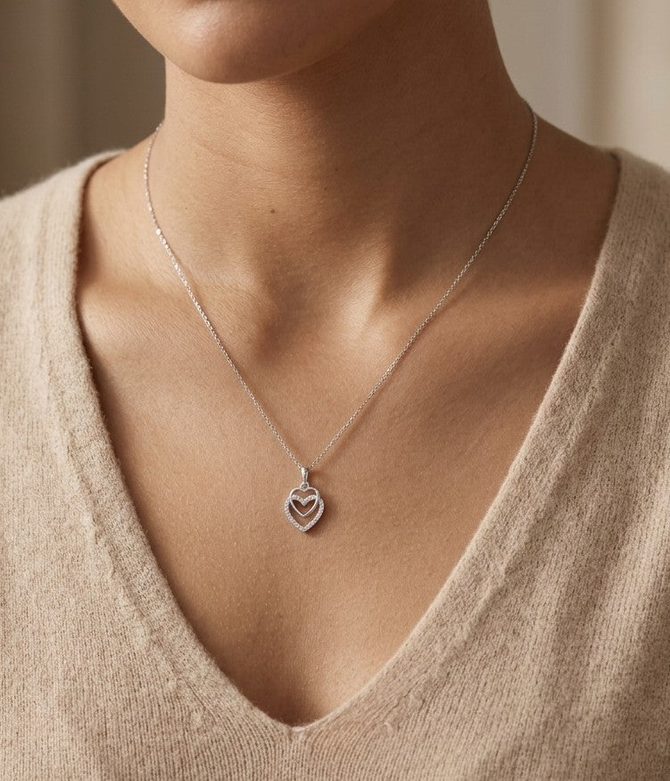 Diamond heart pendant in 18K white gold featuring overlapping open hearts with round brilliant diamond detailing.