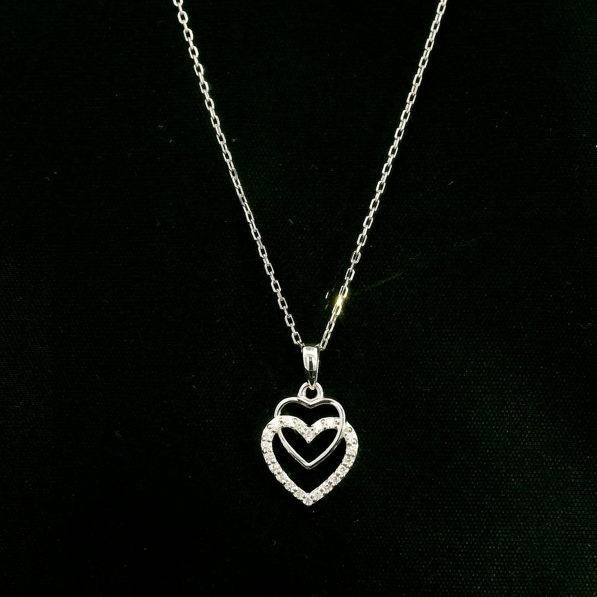 Diamond heart pendant in 18K white gold featuring overlapping open hearts with round brilliant diamond detailing.