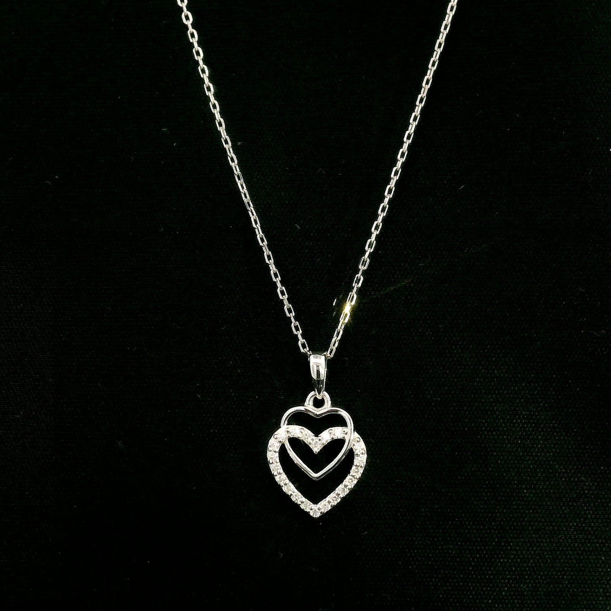 Diamond heart pendant in 18K white gold featuring overlapping open hearts with round brilliant diamond detailing.