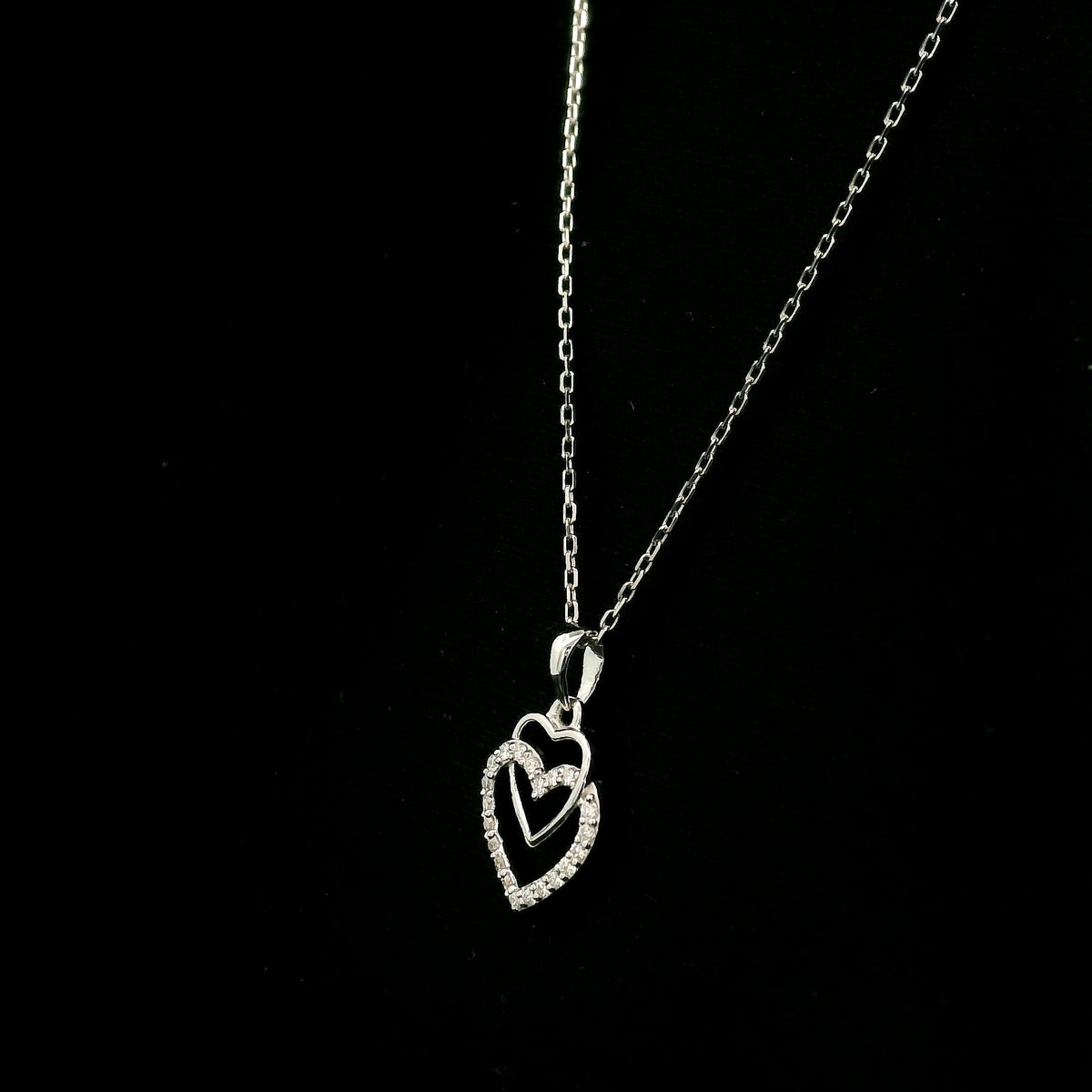 Diamond heart pendant in 18K white gold featuring overlapping open hearts with round brilliant diamond detailing.