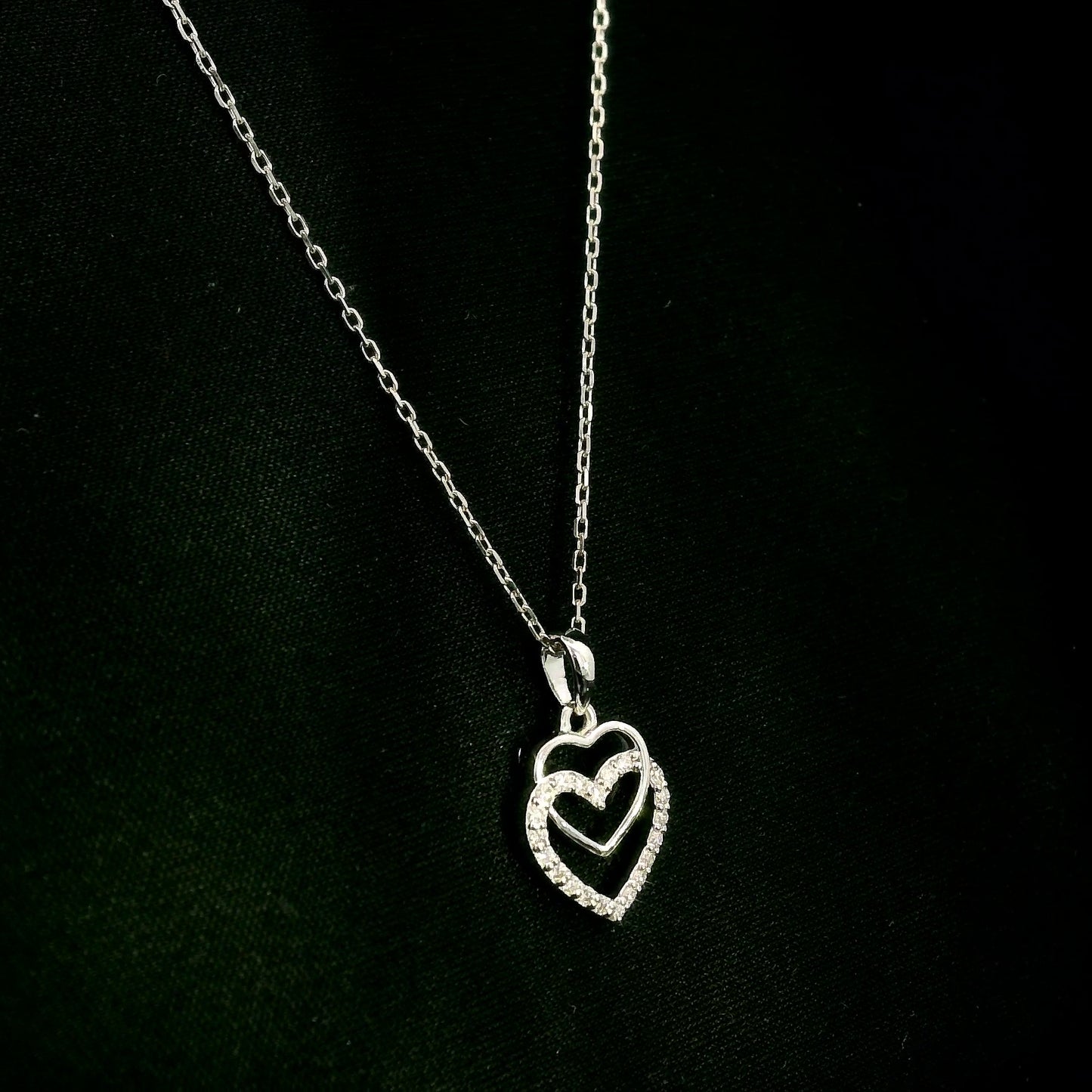 Diamond heart pendant in 18K white gold featuring overlapping open hearts with round brilliant diamond detailing.