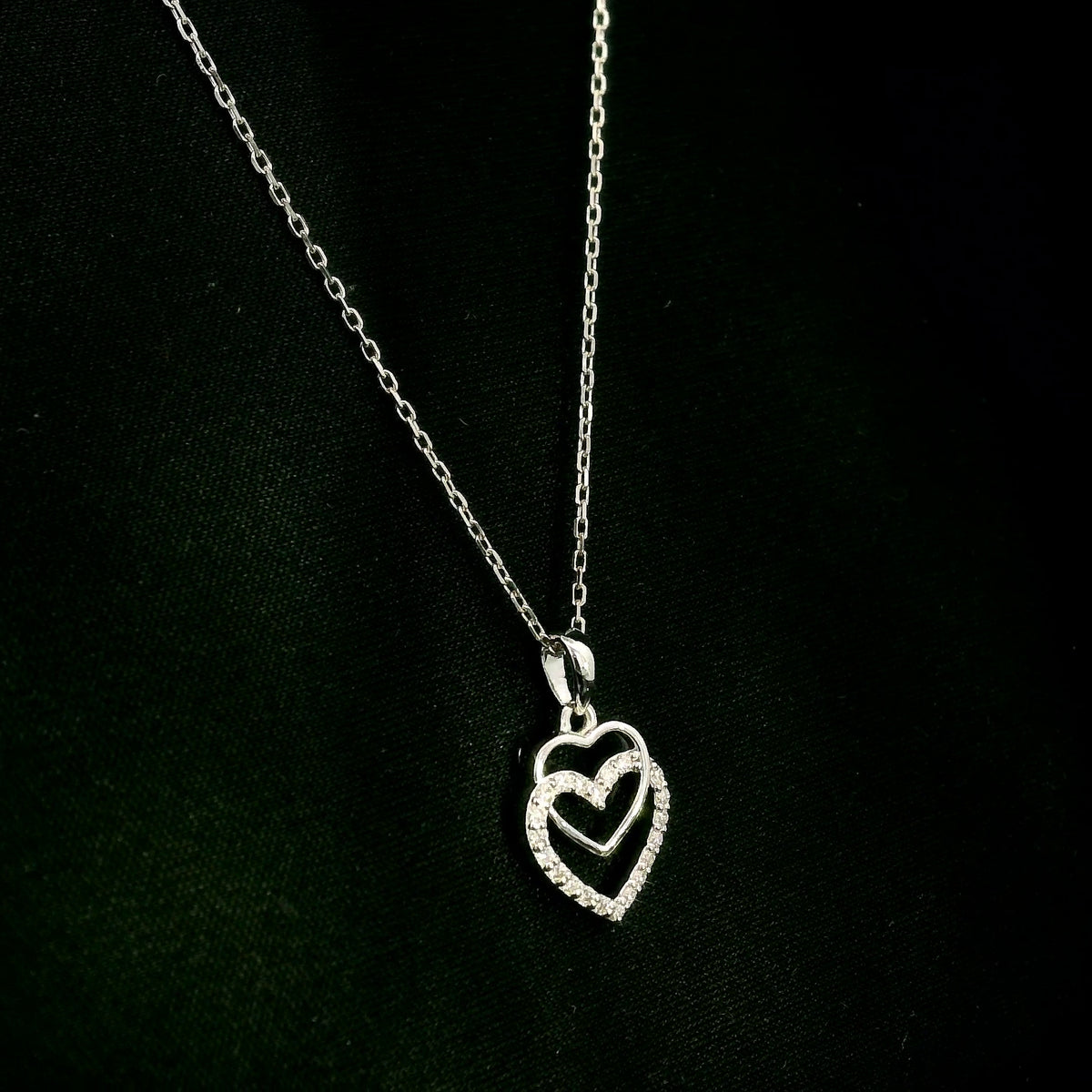 Diamond heart pendant in 18K white gold featuring overlapping open hearts with round brilliant diamond detailing.