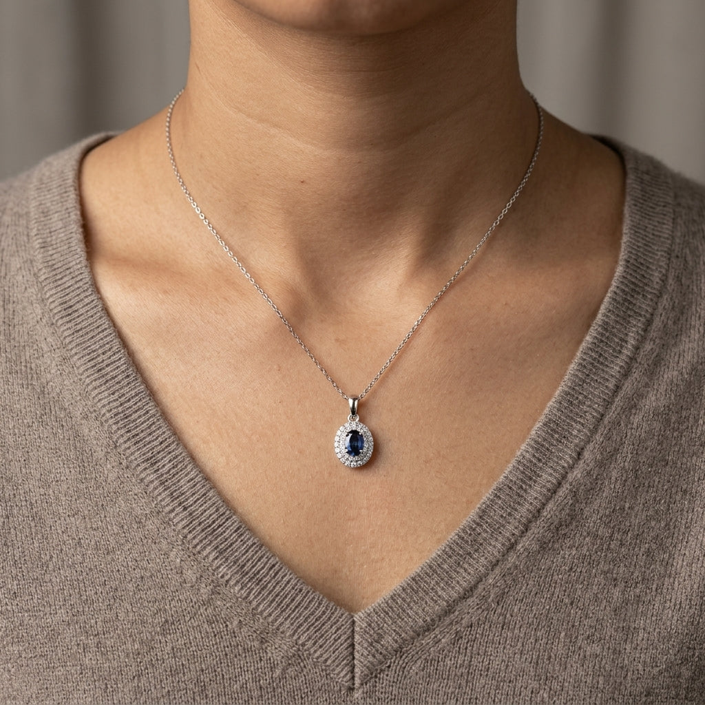 Blue sapphire and diamond halo pendant in 18K white gold with an oval sapphire surrounded by two rows of round diamonds