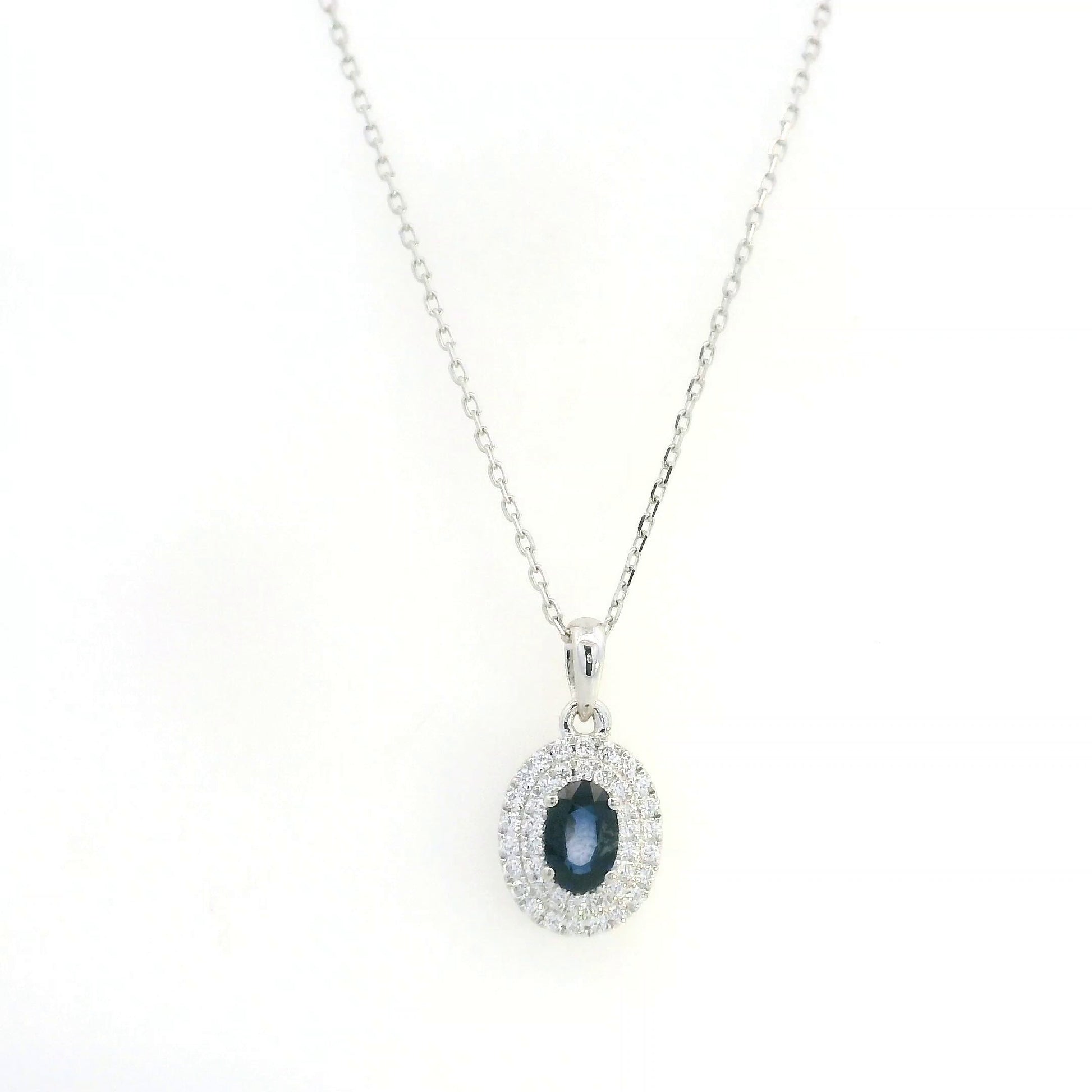 Blue sapphire and diamond halo pendant in 18K white gold with an oval sapphire surrounded by two rows of round diamonds