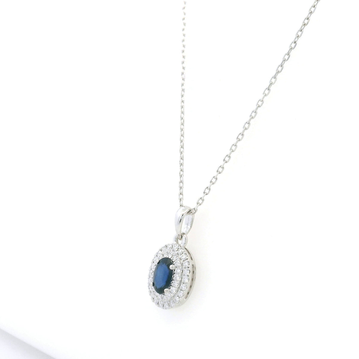 Blue sapphire and diamond halo pendant in 18K white gold with an oval sapphire surrounded by two rows of round diamonds