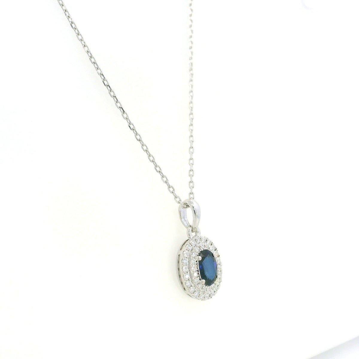 Blue sapphire and diamond halo pendant in 18K white gold with an oval sapphire surrounded by two rows of round diamonds