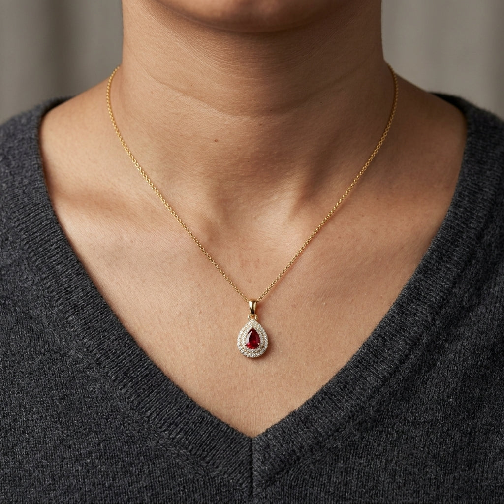 Ruby and diamond halo pendant in 18K yellow gold with a pear-shaped red ruby surrounded by two rows of round diamonds