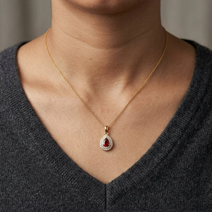 Ruby and diamond halo pendant in 18K yellow gold with a pear-shaped red ruby surrounded by two rows of round diamonds