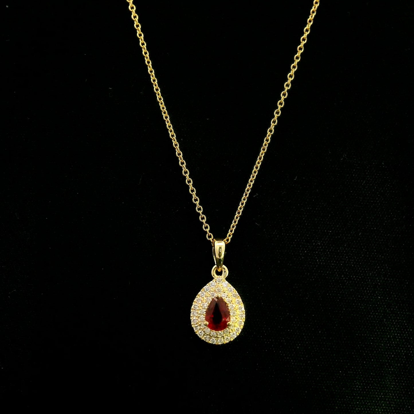 Ruby and diamond halo pendant in 18K yellow gold with a pear-shaped red ruby surrounded by two rows of round diamonds