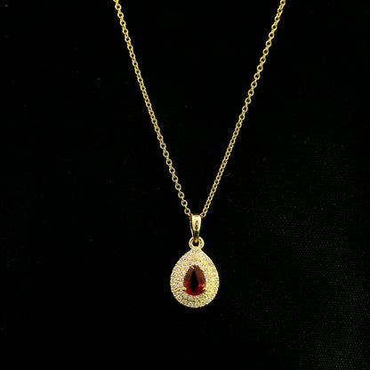 Ruby and diamond halo pendant in 18K yellow gold with a pear-shaped red ruby surrounded by two rows of round diamonds