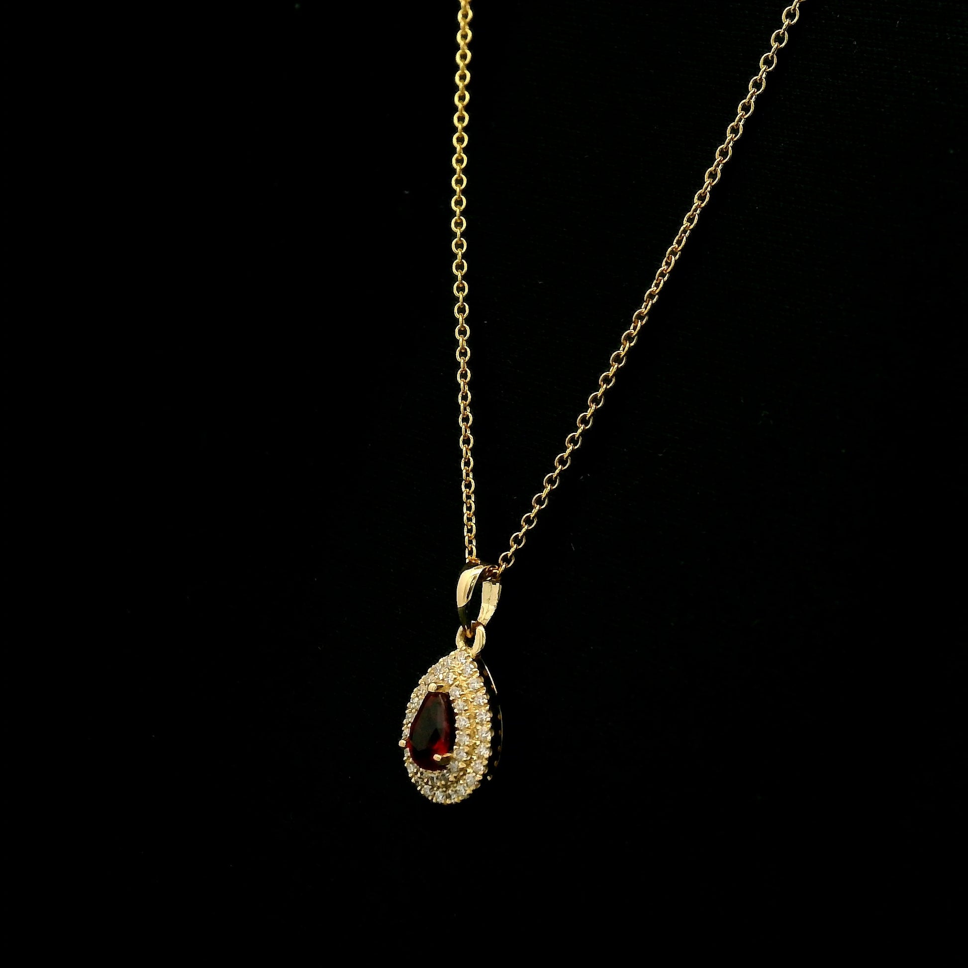 Ruby and diamond halo pendant in 18K yellow gold with a pear-shaped red ruby surrounded by two rows of round diamonds
