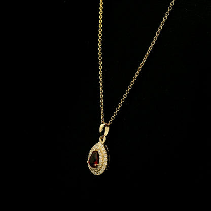 Ruby and diamond halo pendant in 18K yellow gold with a pear-shaped red ruby surrounded by two rows of round diamonds
