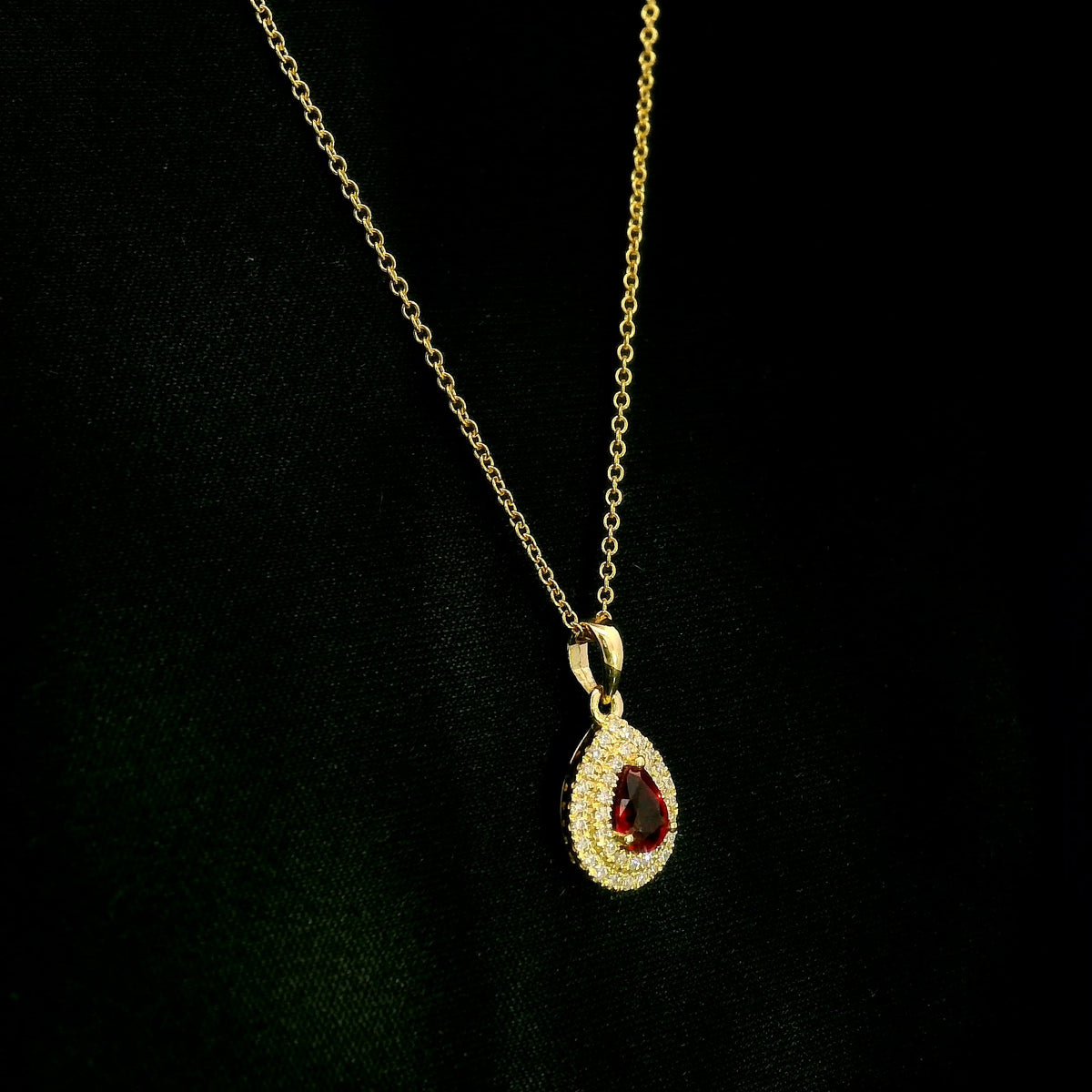 Ruby and diamond halo pendant in 18K yellow gold with a pear-shaped red ruby surrounded by two rows of round diamonds