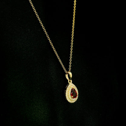 Ruby and diamond halo pendant in 18K yellow gold with a pear-shaped red ruby surrounded by two rows of round diamonds