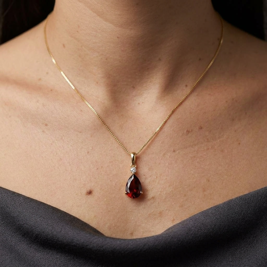 Pear shaped garnet and diamond pendant in 18K yellow gold with a single round diamond accent.