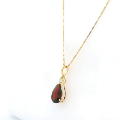 Pear shaped garnet and diamond pendant in 18K yellow gold with a single round diamond accent.