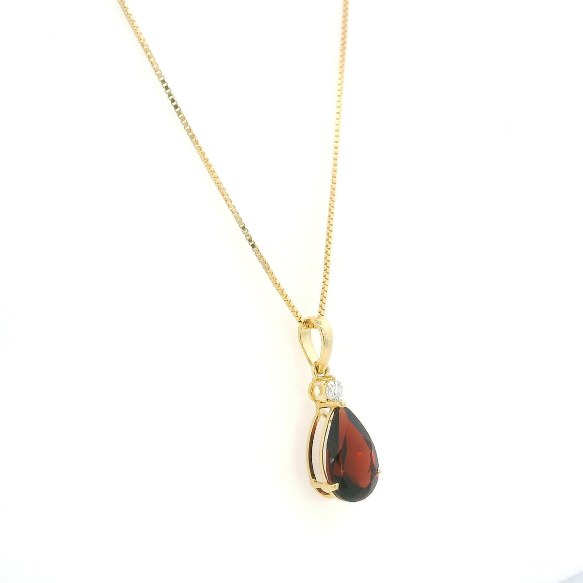 Pear shaped garnet and diamond pendant in 18K yellow gold with a single round diamond accent.