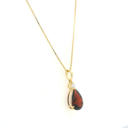 Pear shaped garnet and diamond pendant in 18K yellow gold with a single round diamond accent.