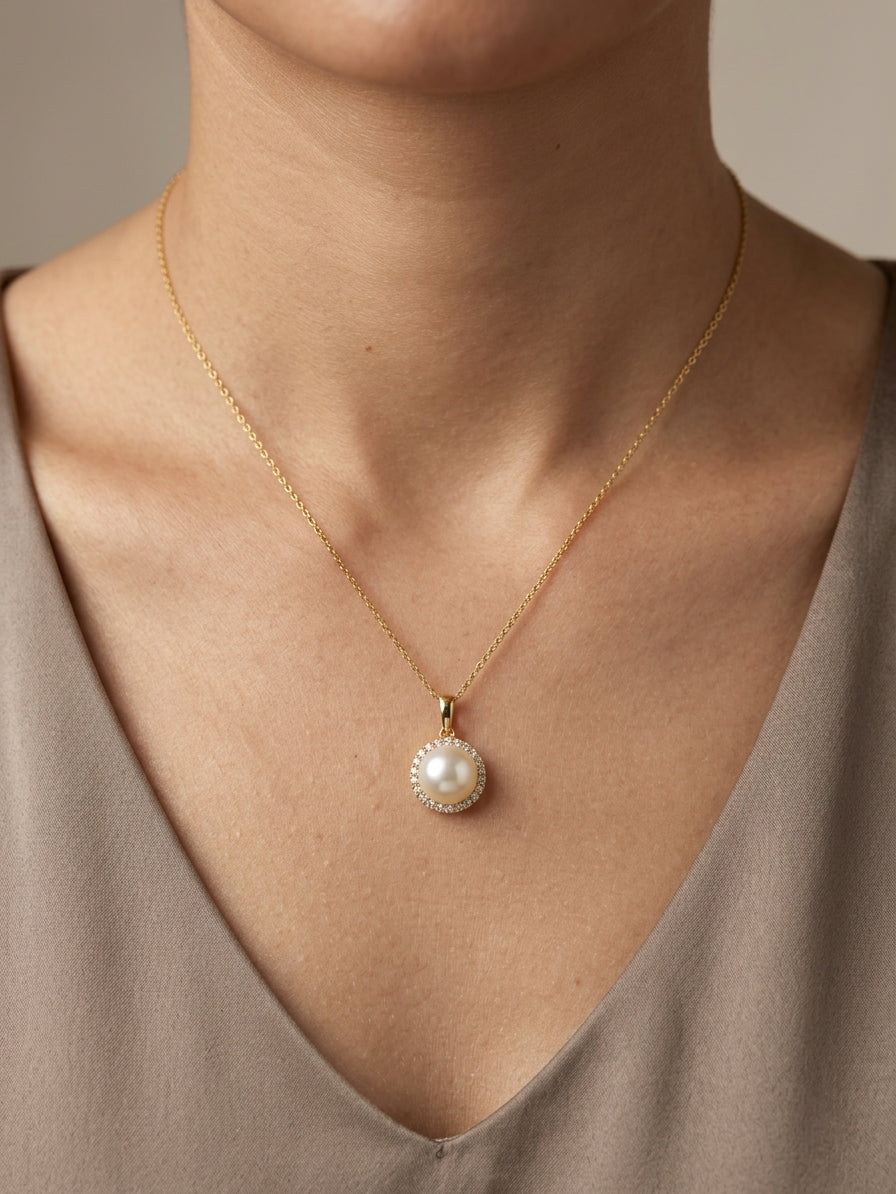 Freshwater white pearl and diamond halo pendant in 18K yellow gold with a round pearl surrounded by brilliant diamonds.