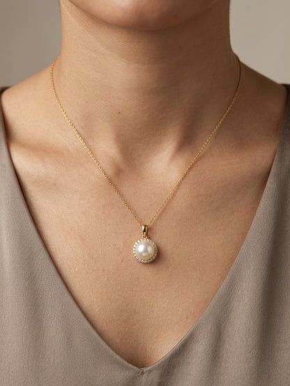 Freshwater white pearl and diamond halo pendant in 18K yellow gold with a round pearl surrounded by brilliant diamonds.