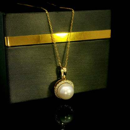 Freshwater white pearl and diamond halo pendant in 18K yellow gold with a round pearl surrounded by brilliant diamonds.