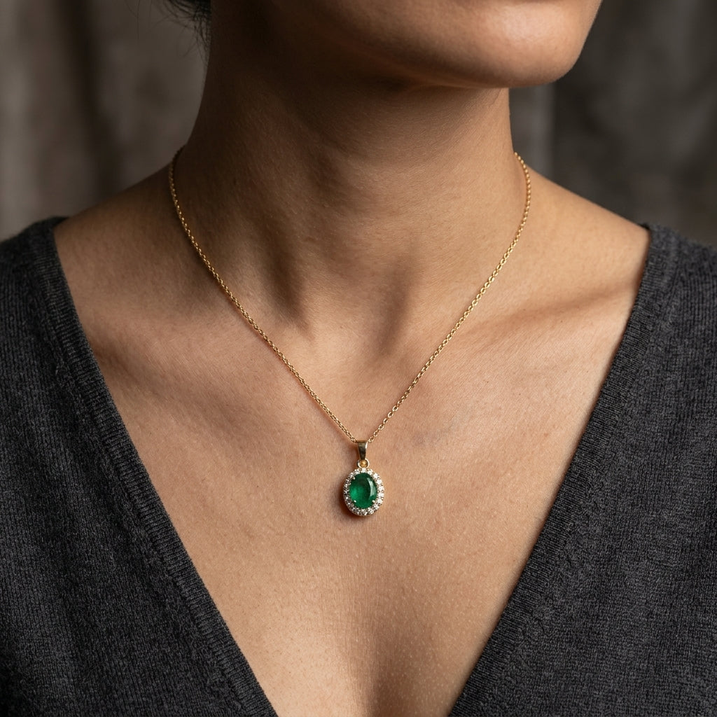 Oval emerald and diamond halo pendant in 18K yellow gold featuring a 1.30 carat green emerald surrounded by round diamonds totalling 0.23 carat. 