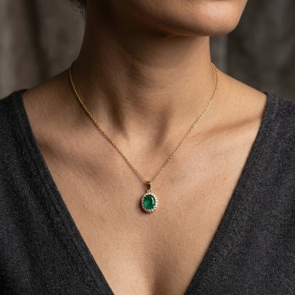 Oval emerald and diamond halo pendant in 18K yellow gold featuring a 1.30 carat green emerald surrounded by round diamonds totalling 0.23 carat. 