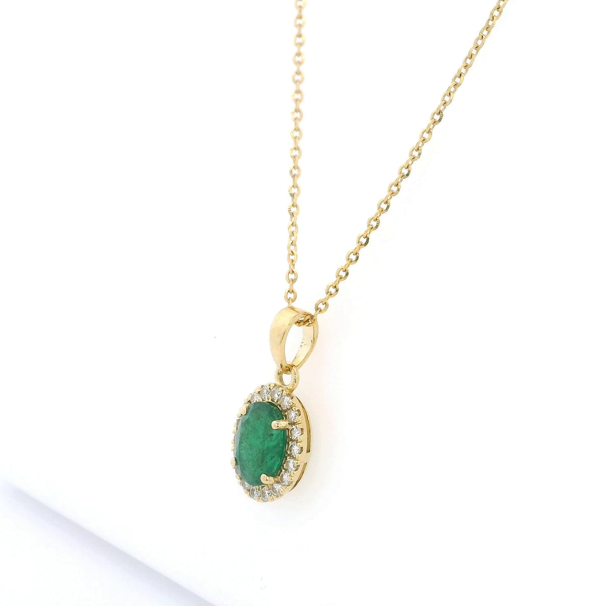Oval emerald and diamond halo pendant in 18K yellow gold featuring a 1.30 carat green emerald surrounded by round diamonds totalling 0.23 carat. 