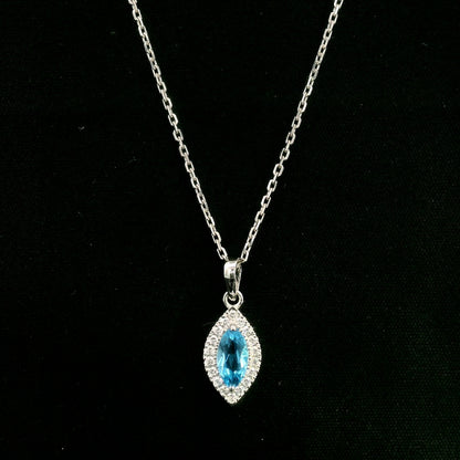 Blue topaz and diamond halo pendant in 18K white gold featuring a 0.70 carat oval blue topaz surrounded by 0.15 carat round diamonds in an elongated marquise-shaped setting, shown with a chain for display.