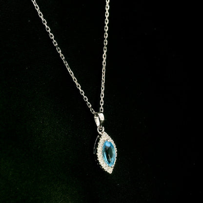 Blue topaz and diamond halo pendant in 18K white gold featuring a 0.70 carat oval blue topaz surrounded by 0.15 carat round diamonds in an elongated marquise-shaped setting, shown with a chain for display.