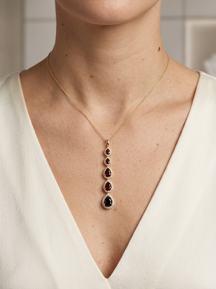 18K yellow gold garnet and diamond drop pendant featuring five pear shaped red garnets totalling 2.26 carats, each surrounded by a halo of round diamonds totalling 0.36 carat. Chain not included.