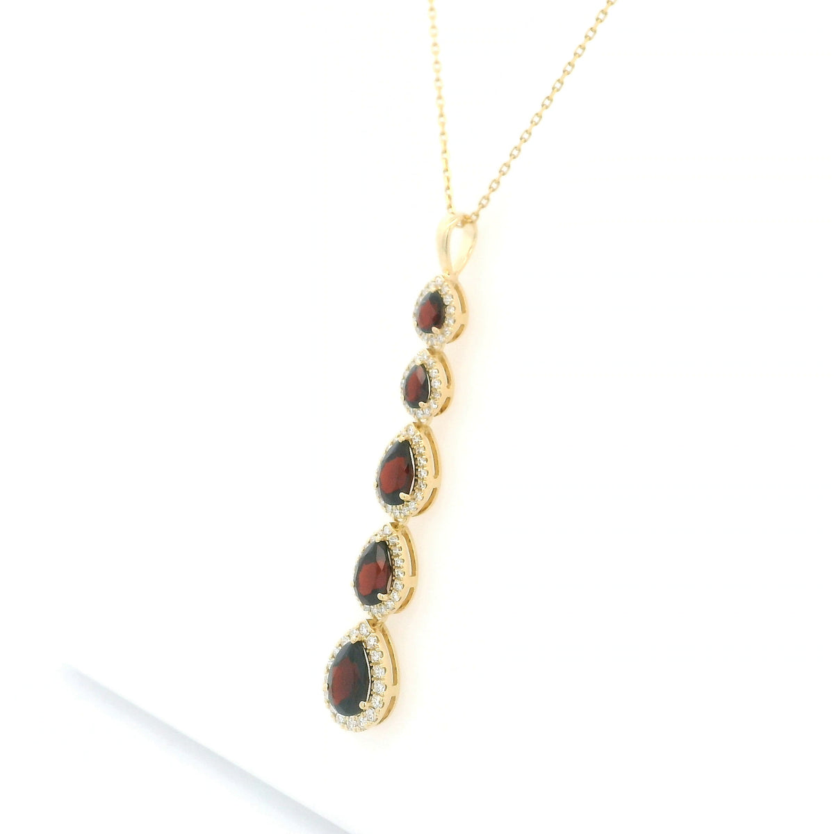 18K yellow gold garnet and diamond drop pendant featuring five pear shaped red garnets totalling 2.26 carats, each surrounded by a halo of round diamonds totalling 0.36 carat. Chain not included.