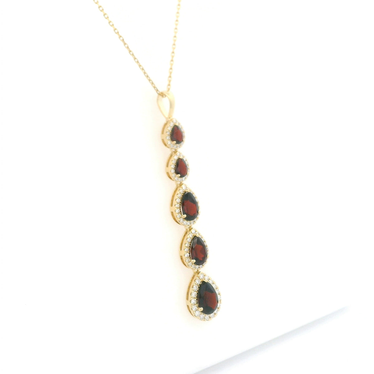 18K yellow gold garnet and diamond drop pendant featuring five pear shaped red garnets totalling 2.26 carats, each surrounded by a halo of round diamonds totalling 0.36 carat. Chain not included.