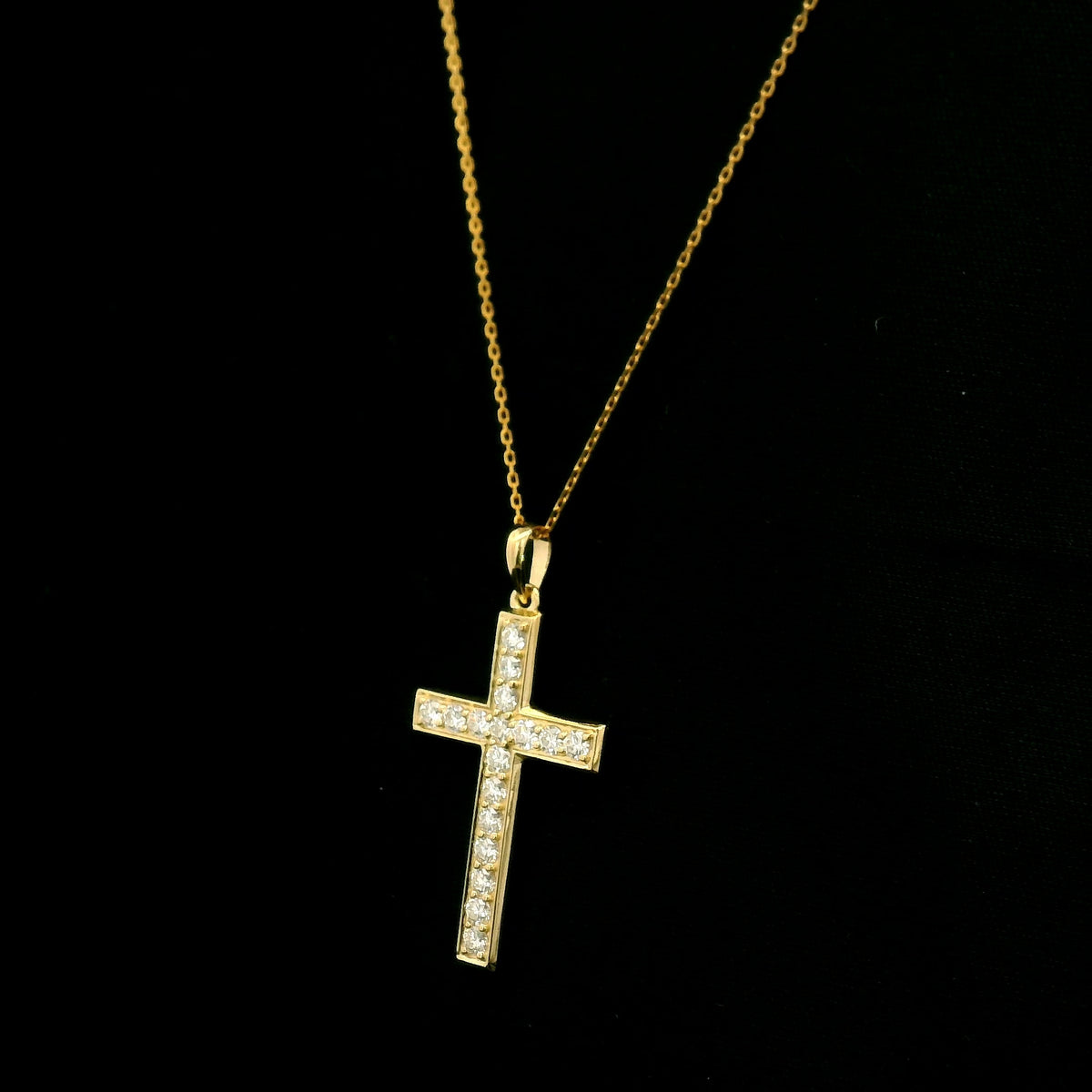 18K yellow gold Christian cross pendant with round diamonds set along the vertical and horizontal arms, shown hanging from a fine gold chain.