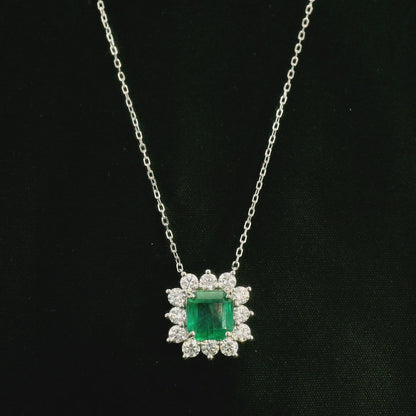 Emerald and diamond cluster halo necklace in 18K white gold featuring a 2.53 carat rectangular emerald surrounded by round diamonds totalling 1.46 carats, suspended from a fine white gold chain.