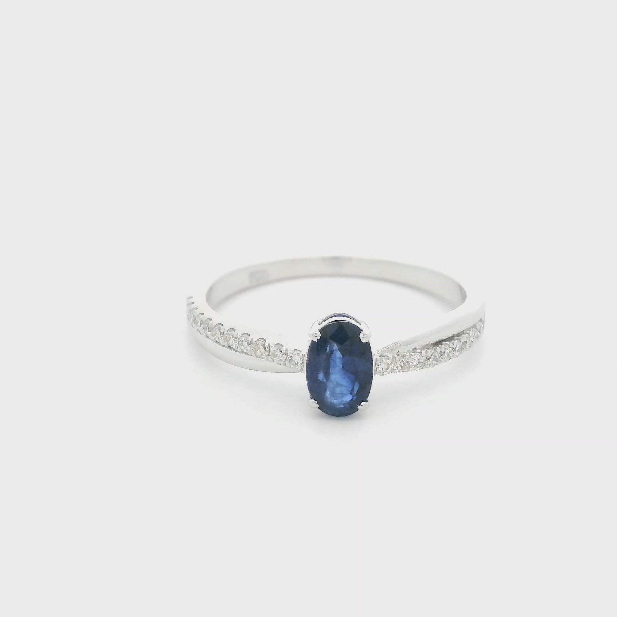 Oval blue sapphire ring with diamond-set shoulders in polished 18K white gold, featuring a four-prong centre gemstone setting.