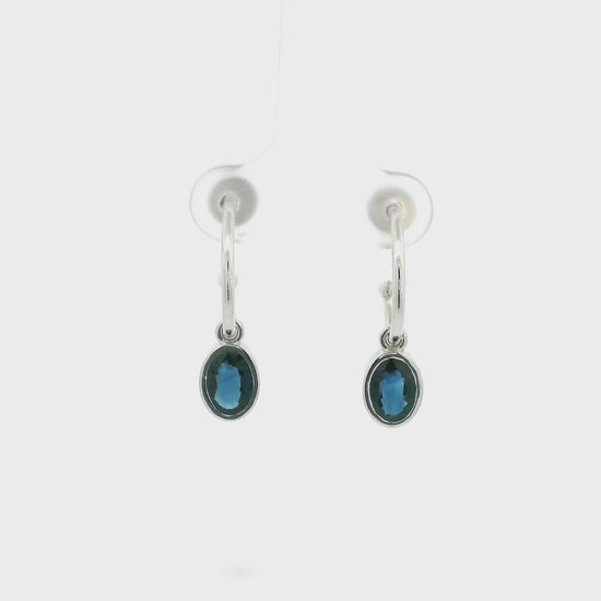 Oval blue sapphire drop hoop earrings in 18K white gold with polished hoops and suspended sapphire drops.