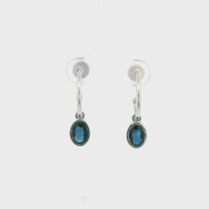 Oval blue sapphire drop hoop earrings in 18K white gold with polished hoops and suspended sapphire drops.