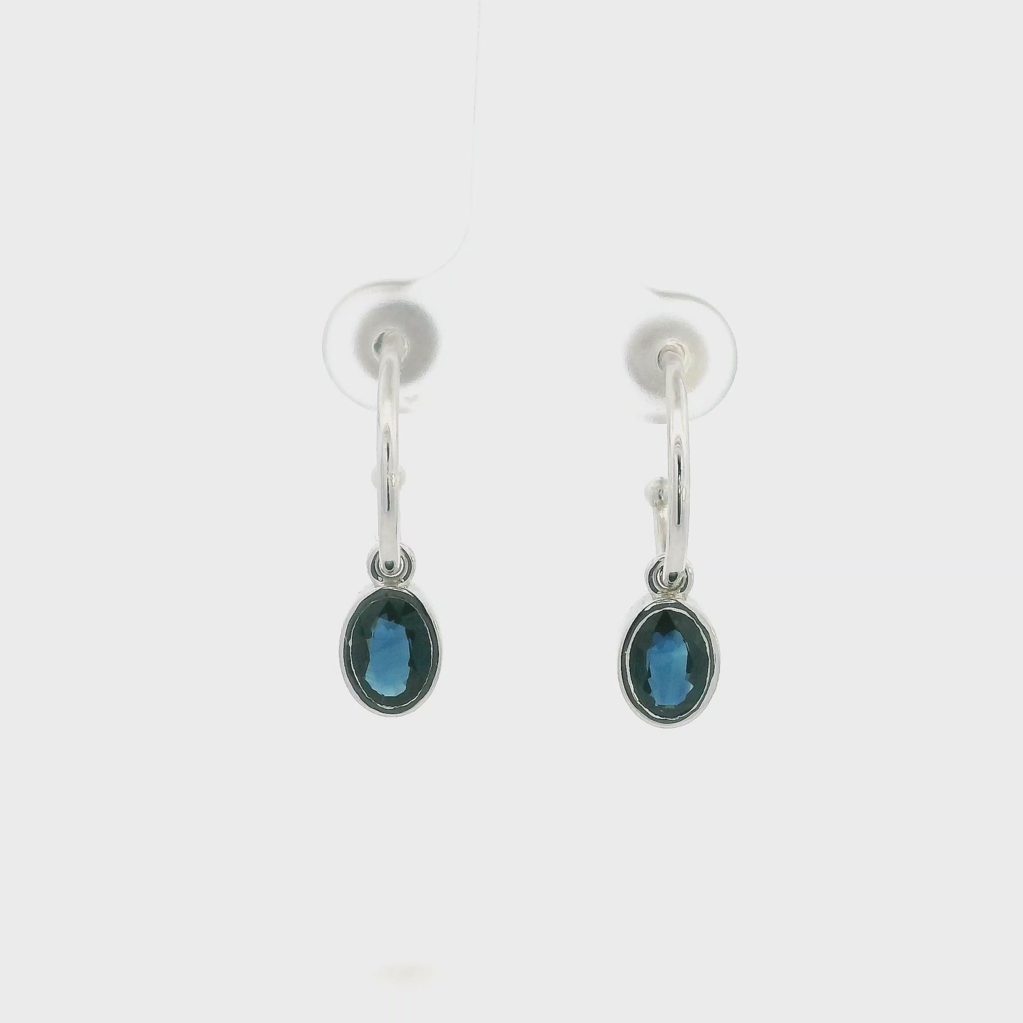 Oval blue sapphire drop hoop earrings in 18K white gold with polished hoops and suspended sapphire drops.